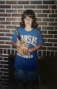 Ryan Sallans as a teenage girl holding a softball mitt and trophy.